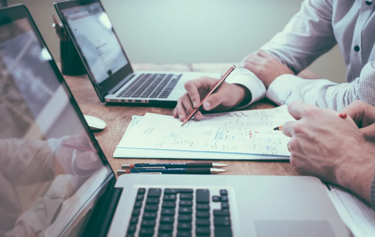 imagem ilustrativa de um notebook na mesa com pessoas fazendo cálculos sobre receitas e investimentos