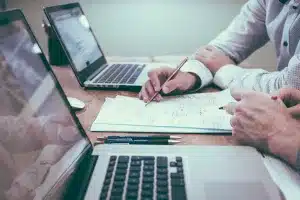 imagem ilustrativa de um notebook na mesa com pessoas fazendo cálculos sobre receitas e investimentos